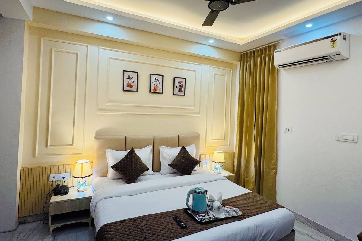Una habitación de hotel con cama, lámparas de noche, ventilador de techo, aire acondicionado y obras de arte enmarcadas en la pared.