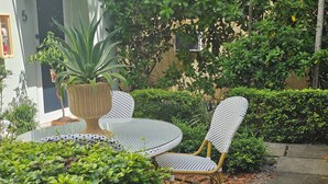 Een terras met rieten meubilair, een plant in pot en een haag.