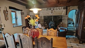 A dining area with a wooden table, chairs, and a vase with flowers. There is a stone fireplace and a mirror on the wall. - Breton house in the heart of the Monts d'Arrée   (Scrignac)