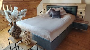 A bedroom with a wooden ceiling, a bed with white bedding, two pillows, a nightstand, a lamp, and a painting on the wall. - Breton house in the heart of the Monts d'Arrée   (Scrignac)