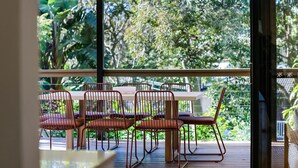 Un espace repas avec une table et des chaises, offrant une vue sur une végétation luxuriante grâce à de grandes fenêtres.