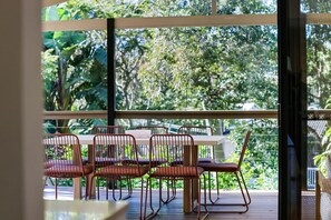 Un comedor con mesa y sillas, y vista a exuberante vegetación a través de amplios ventanales.