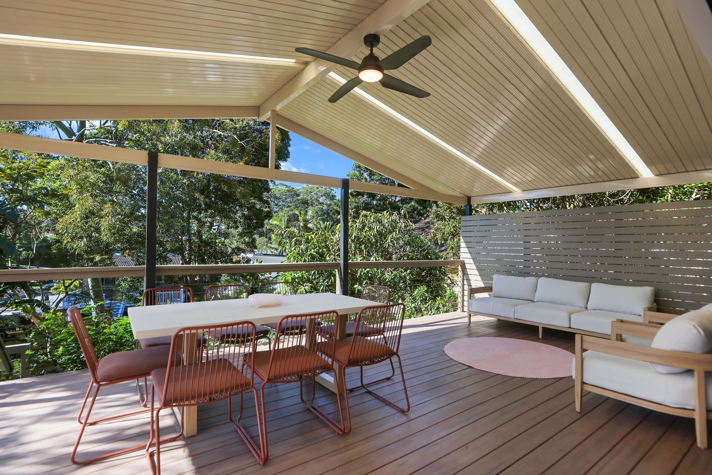 An outdoor patio with a table and chairs, a sofa, and a ceiling fan.
