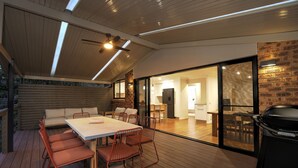 Un espace extérieur aménagé pour les repas, avec une terrasse en bois, une table et des chaises, ainsi qu’un barbecue.