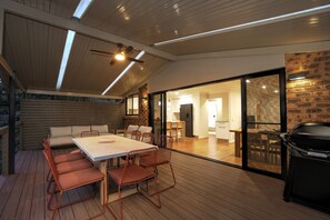 Un área de comedor al aire libre con terraza de madera, una mesa con sillas y una parrilla.