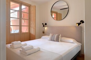 A hotel room with a bed, a round mirror, two wall-mounted lamps, and a view through a door with a window. - Thyssen Terrace Apartment (Málaga)