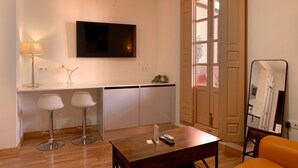 Una sala de estar moderna con un televisor de pantalla plana montado en la pared, una mesa de centro de madera con controles remotos, dos taburetes altos y un ventanal con vistas.