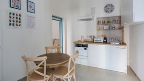 Cocina compacta con armarios blancos, encimera de madera y lavavajillas integrado. Se observan cuadros enmarcados en la pared y un accesorio de iluminación en el techo.