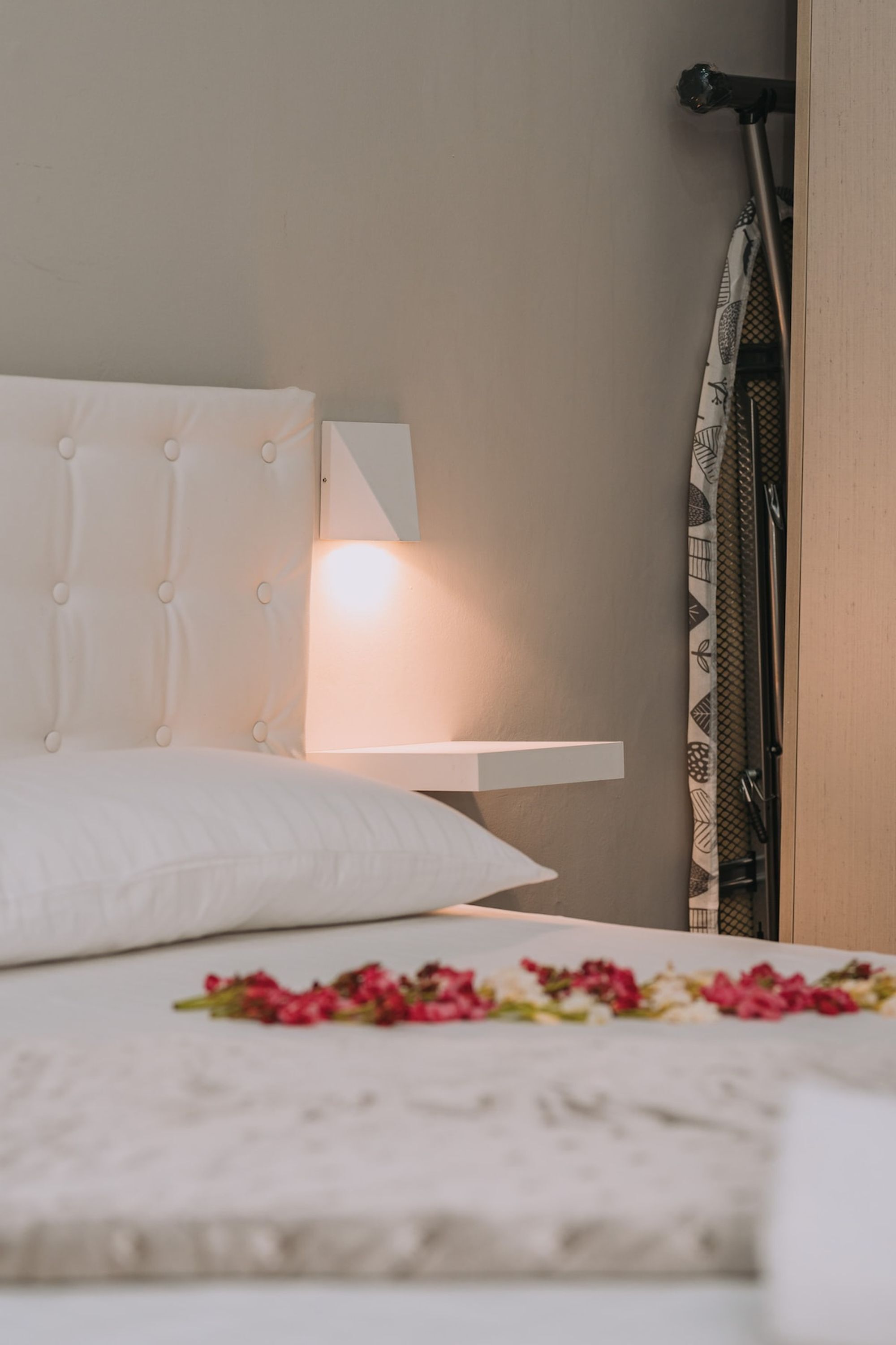 En pænt redt seng med et hvidt sengegærde, et natbord med en lampe og en blomsterdekoration på sengen.