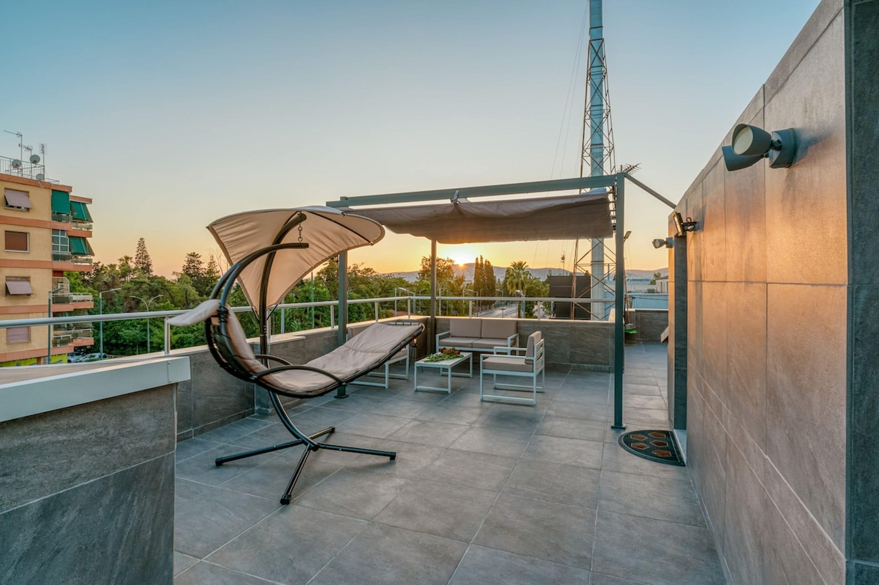 A rooftop terrace with a cushioned chair, a small table, and a covered seating area.