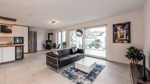 A modern living room with a black sofa, a coffee table, and a large window offering a view of a residential area.