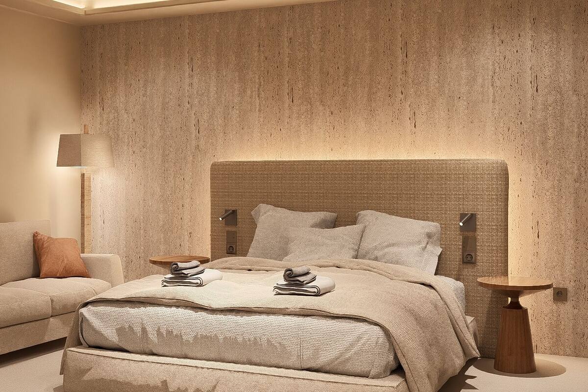 A bedroom with a large bed, a bedside table, a lamp, and a mirror on the wall.