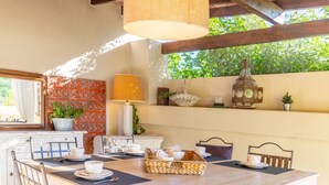 A dining area with a wooden table, chairs, a hanging light fixture, a potted plant, and a decorative wall piece.