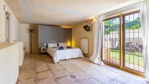 A bedroom with a bed, a bedside table, a lamp, a radiator, and a sliding glass door to a patio.