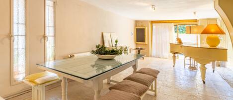 A dining area with a glass table, benches, a piano, and a potted plant.