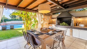 An outdoor kitchen with a stone wall, a grill, and a dining area with chairs and a table.