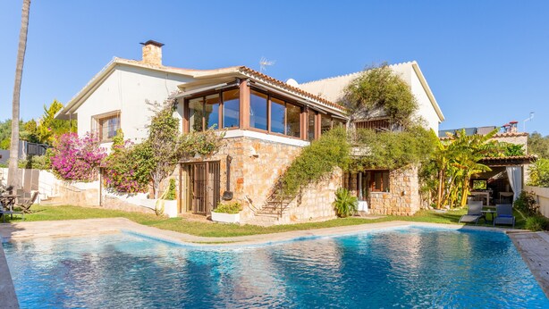 A house with a swimming pool, stone walls, and a large window.