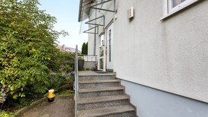 A residential building with a concrete staircase leading to a door, surrounded by greenery.