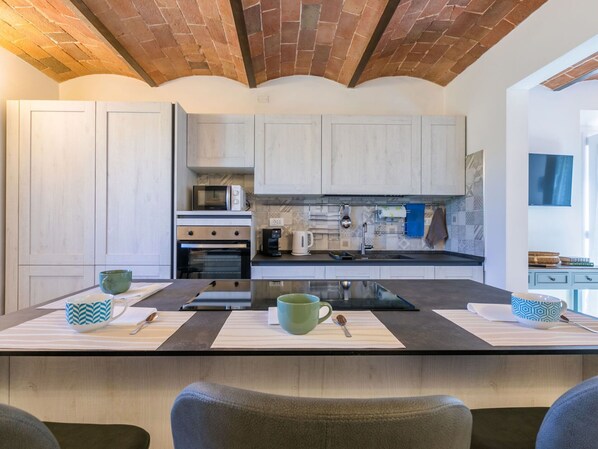 Cocina moderna con armarios de madera clara, techo de ladrillo y una isla central con dos tazas verdes.