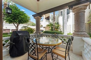 Une terrasse extérieure couverte, avec une table ronde et des chaises, un barbecue et une vue sur un bâtiment blanc orné de colonnes.