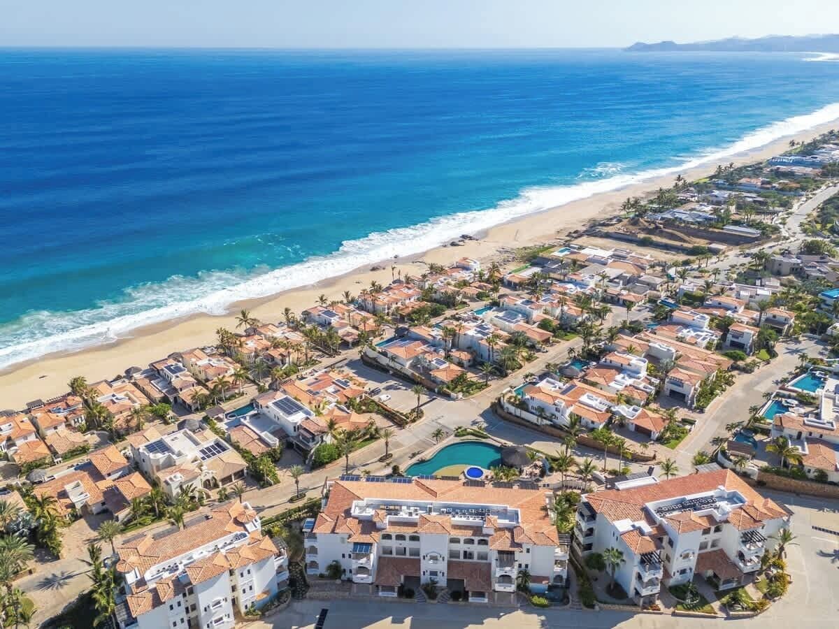 Vista aérea de una zona residencial costera con casas, una playa y una piscina.