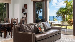 A living room with a brown leather sofa, a dining table with chairs, and a view of the ocean through large sliding glass doors. - Luxurious Ocean View Retreat at El Encanto! (San Jose del Cabo)