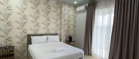 A bedroom with a large bed, a chandelier, a small table with a vase, and a window with curtains.