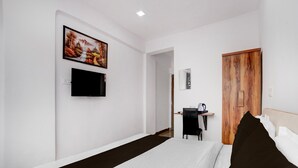A hotel room with a bed, a desk, a chair, a television, and a wooden door. - Classic Laxmi Chowk Hinjewadi (Paud)