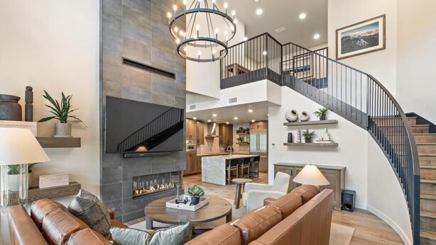 A spacious living area with a curved staircase, leather seating, a fireplace, and a modern kitchen in the background. - Edge Of Powder | Includes Two 1-Day Lift Tickets (Tamarack)