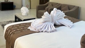 A hotel room with a neatly made bed, a sofa, a small table with a decorative item, a television, and a kitchenette in the background. - Rest inn (Madinah)