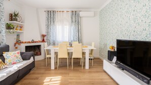 A living room with a sofa, TV, dining table, chairs, fireplace, and decorative plants. - Charming Holiday Home 'Can Dornena Refugio' with Mountain View, Wi-Fi & Air Conditioning (Maçanet de la Selva)