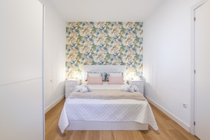 A bedroom with a bed, nightstands, a headboard with a floral pattern, and a wall with a tropical leaf design.