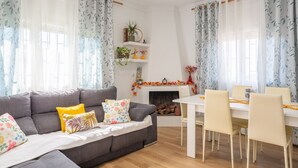 A living room with a gray sofa, a white dining table, and chairs. There is a fireplace with a mantel decorated with plants and a garland. - Charming Holiday Home 'Can Dornena Refugio' with Mountain View, Wi-Fi & Air Conditioning (Maçanet de la Selva)