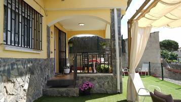 Una casa de fachada de piedra, con un balcón que tiene una mesa y sillas, y un patio cercado con césped artificial.