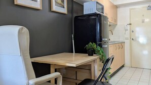 Cozinha compacta com geladeira, micro-ondas e pequeno espaço de refeições com uma cadeira e mesa.