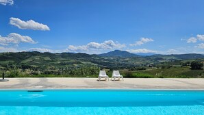 Une piscine avec deux chaises longues blanches, offrant une vue sur des collines et des montagnes verdoyantes sous un ciel dégagé.