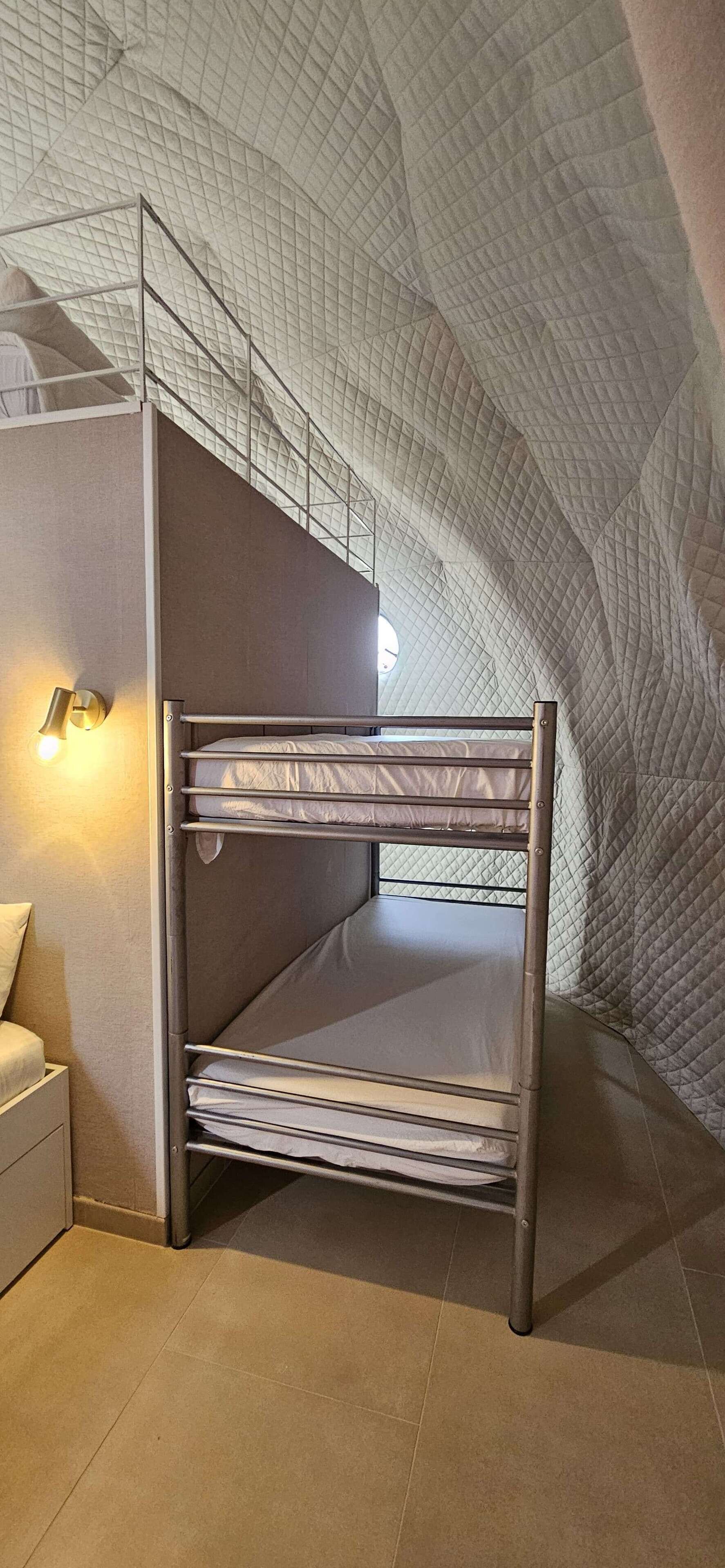 Een stapelbed in een kamer met een bijzondere gewelfde plafond, een bedlampje en een klein nachtkastje.