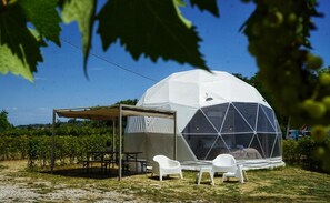 Estrutura em cúpula geodésica com área de varanda coberta e duas cadeiras brancas.
