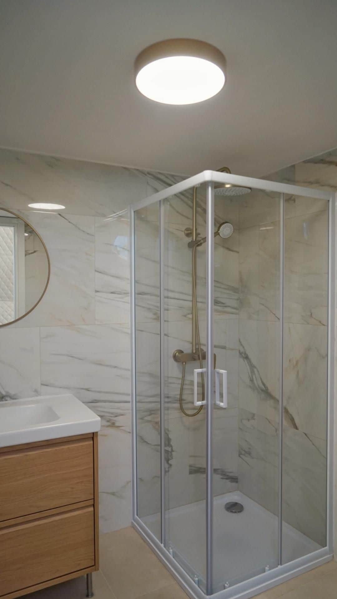 A modern bathroom with a glass-enclosed shower, marble walls, and a wooden vanity.