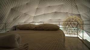 Un lit doté d’un baldaquin matelassé et d’un luminaire au design géométrique placé au-dessus.