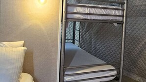 Un lit superposé avec une structure en métal et une literie blanche, un luminaire fixé au mur et un mur texturé à motifs matelassés.