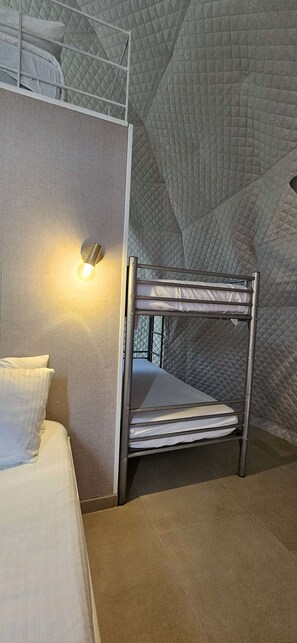A bunk bed with a metal frame and white bedding, a wall-mounted light, and a textured quilted wall. - Cozy Cabin Retreat in Ortezzano (Ortezzano)