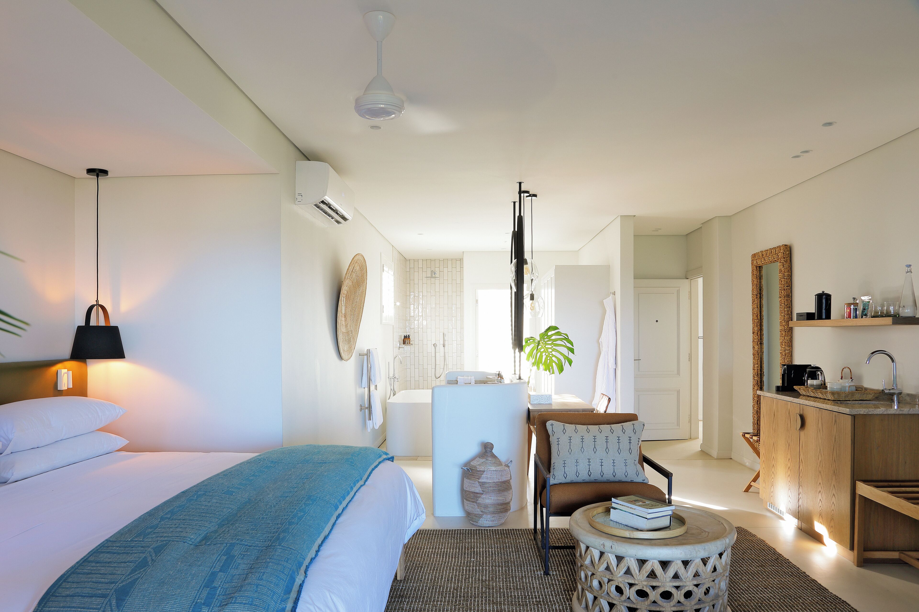 A modern hotel room with a bed, a small seating area, a bathroom, and a kitchenette.