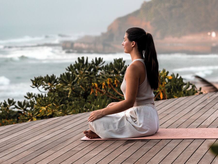 A person meditating on a wooden deck with a view of the ocean and hills.