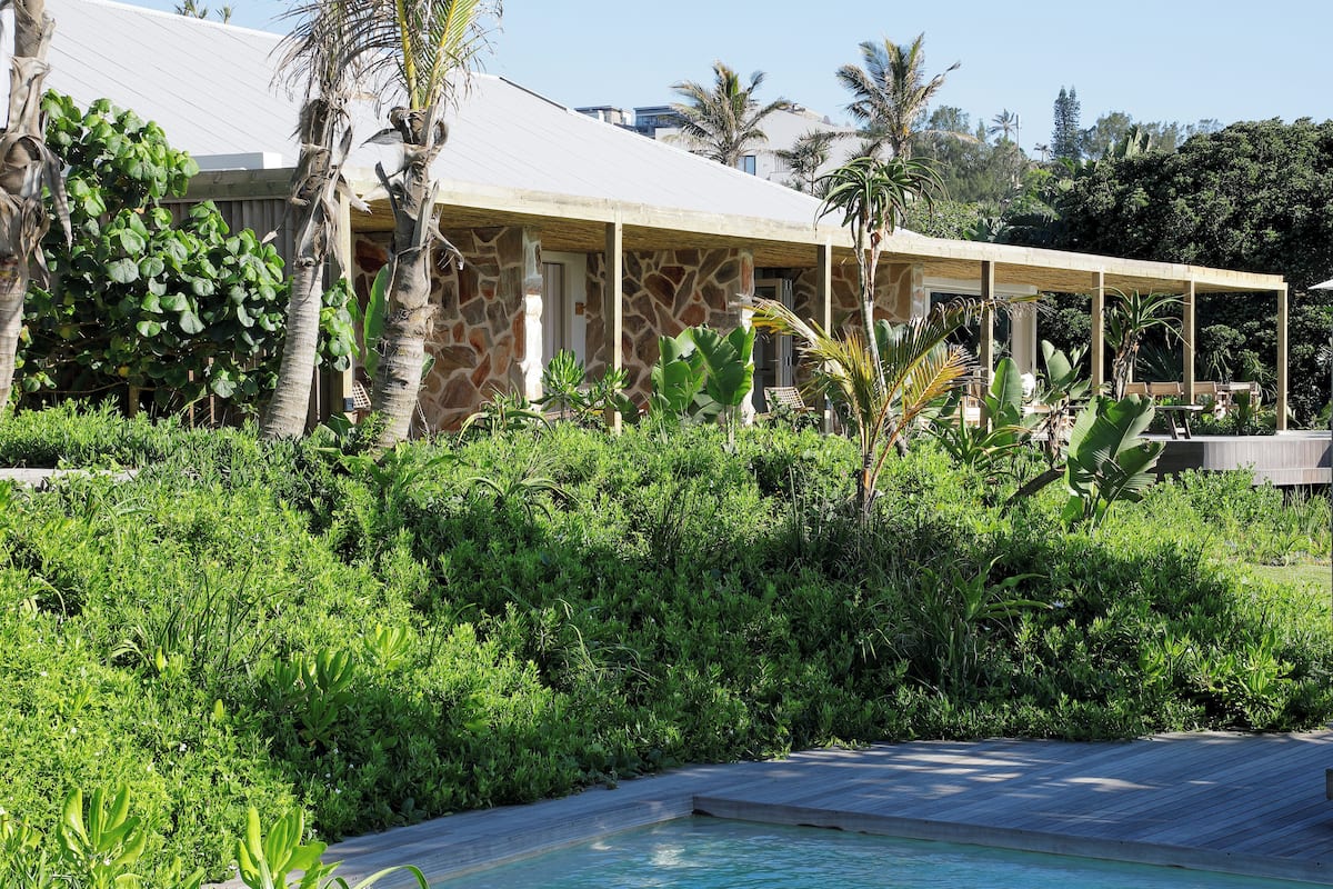 A pool area with a stone building and a covered seating area.
