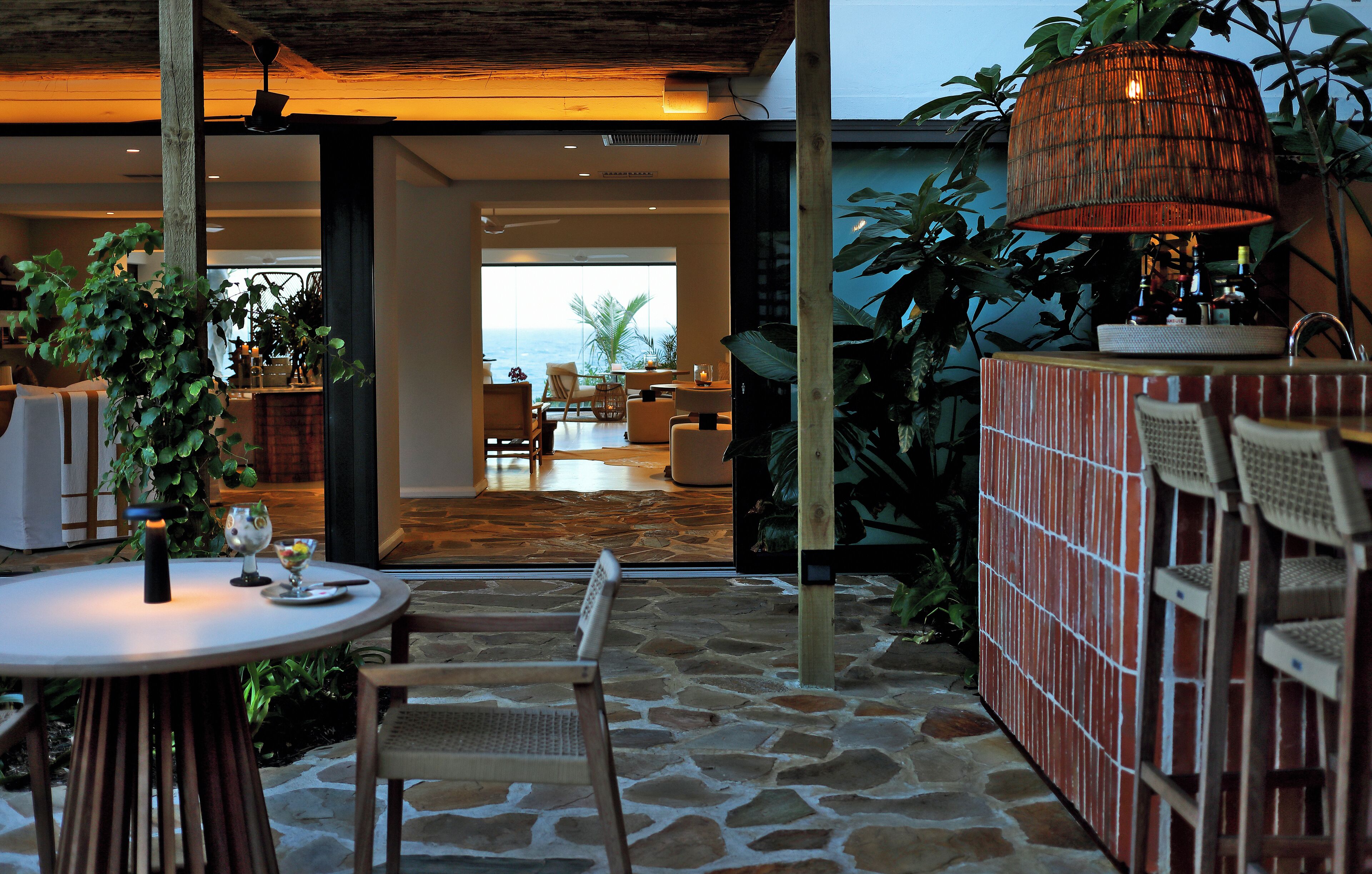 An outdoor patio with stone flooring, a round table with chairs, a hanging lamp, and a brick wall with seating.