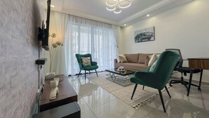 Un salon moderne comprenant un canapé, deux fauteuils, une table basse et un téléviseur fixé au mur.