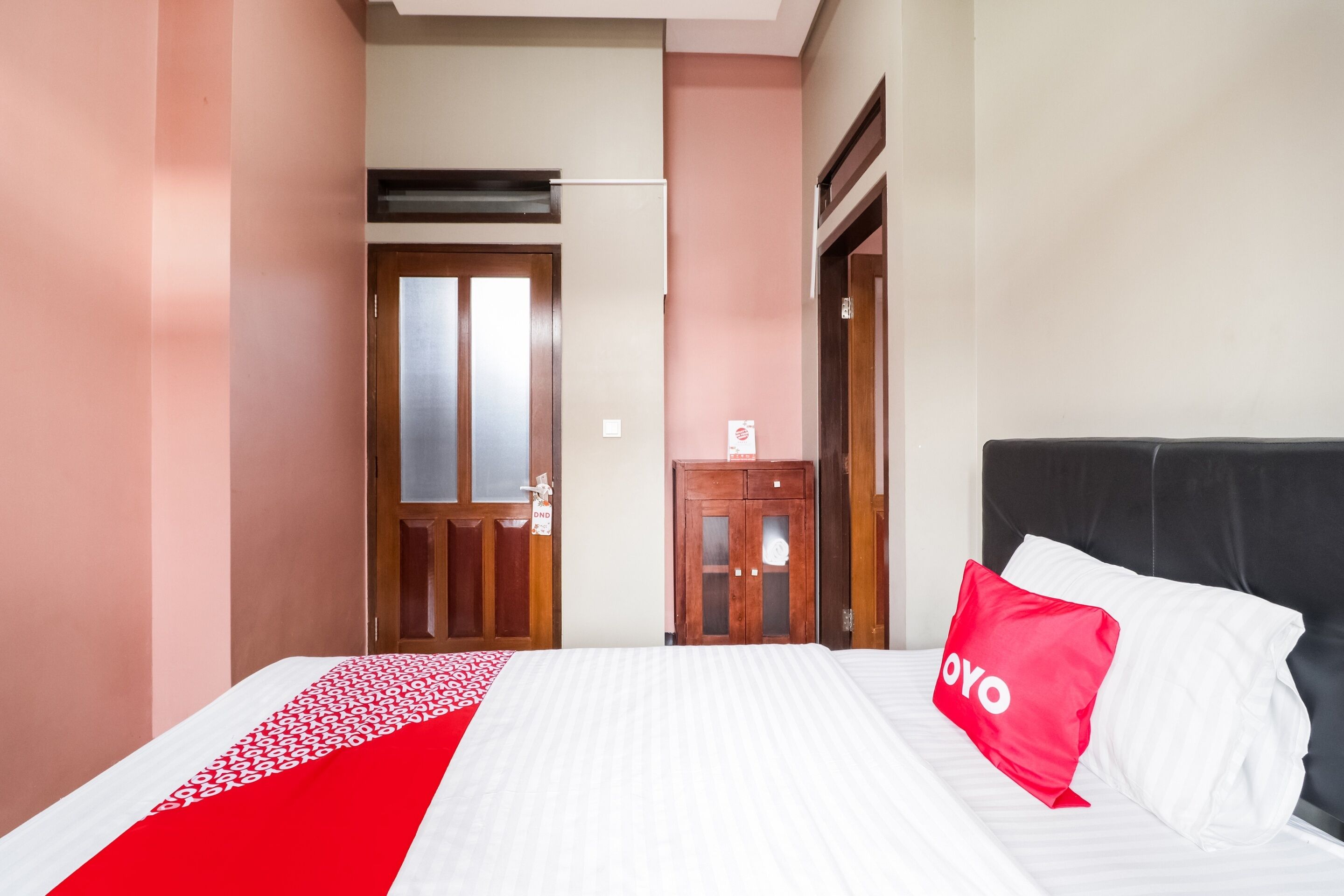 Ein Hotelzimmer mit einem Bett, einer rot-weißen Bettdecke, einem roten Kopfkissen mit der Aufschrift "YOYO" und einem hölzernen Kleiderschrank.