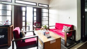 A modern living room with a red sofa, wooden coffee table, and a small side table. There are two chairs, a window with blinds, and a door with a glass panel. - Hotel O Guest House Teras Waruga Syariah (Parongpong)