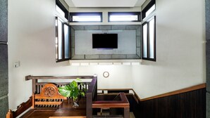 A modern interior with a wooden dining table, a bench, and a flat-screen TV mounted on a stone wall. - Hotel O Guest House Teras Waruga Syariah (Parongpong)